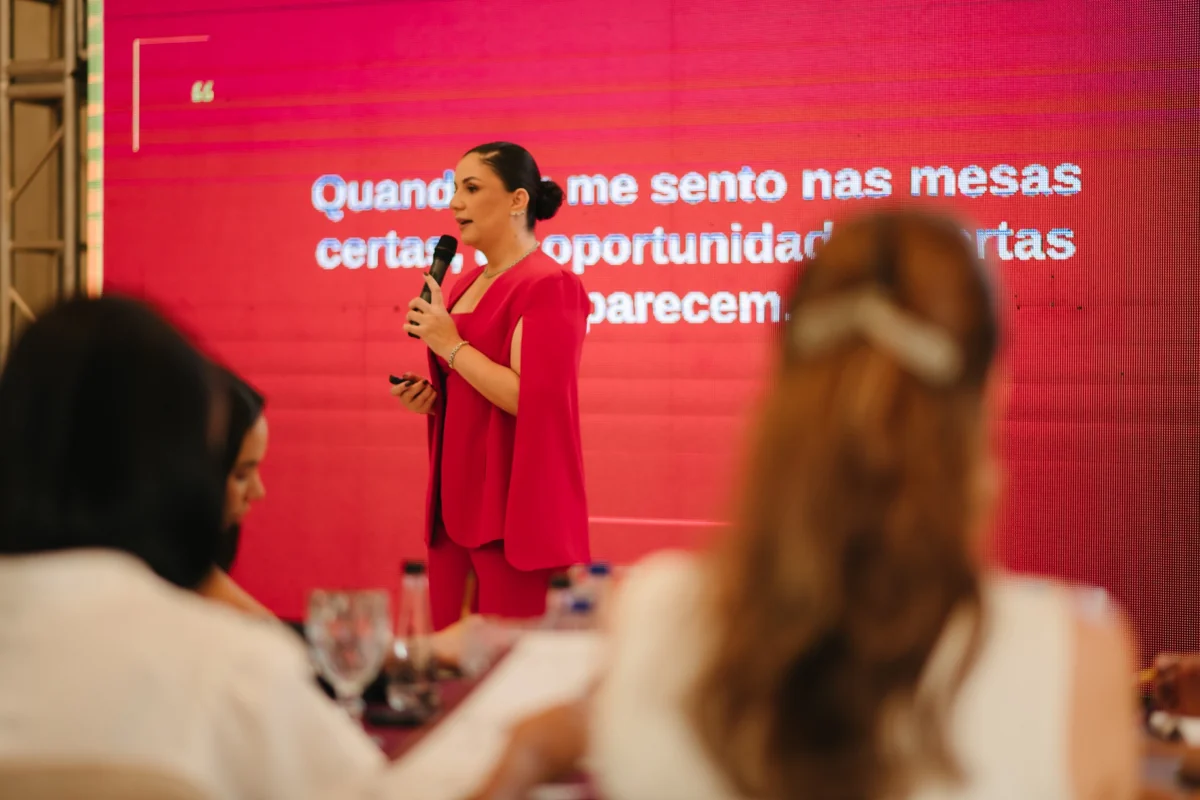 Lilian Arcanjo com microfone, conduzindo uma apresentação diante das participantes